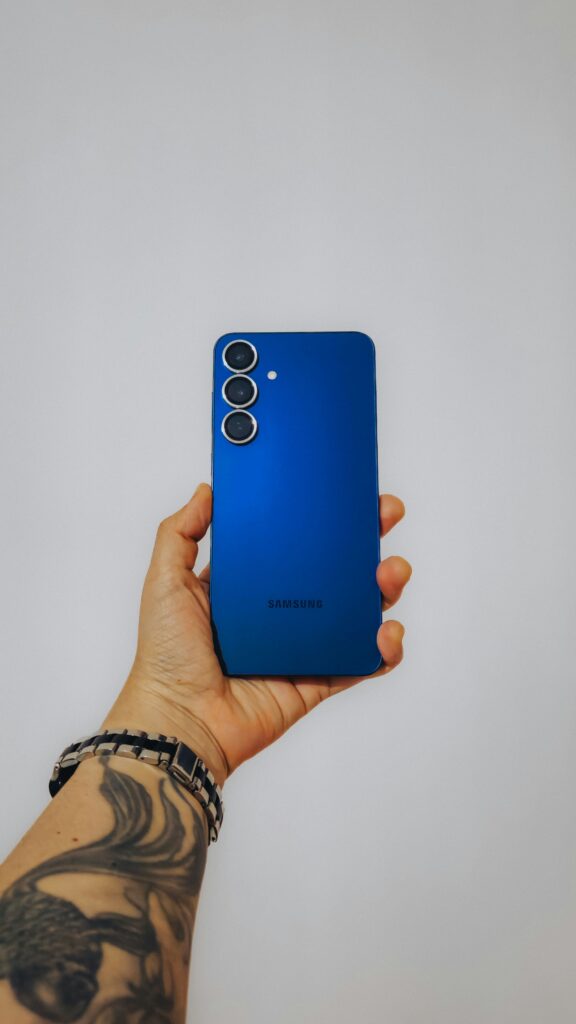 Blue smartphone held by tattooed hand, isolated on white for a modern and clean look.